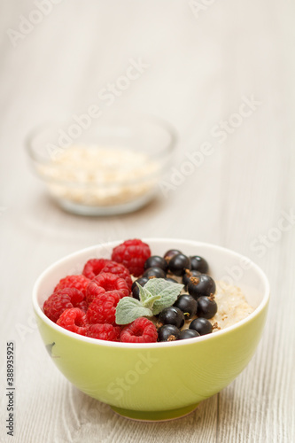 Oatmeal porridge in porcelain bowl with currant berries and raspberries