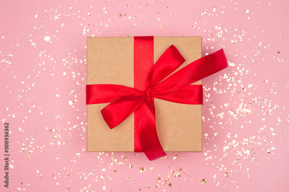 Present box with red bow on festive pink background with golden sparkles around and copyspace for your text. Flat lay style. Christmas, New Year, Valentines Day or birthday celebration concept Present box with red bow on festive pink background with golden sparkles around and copyspace for your text. Flat lay style. Christmas, New Year, Valentines Day or birthday celebration concept