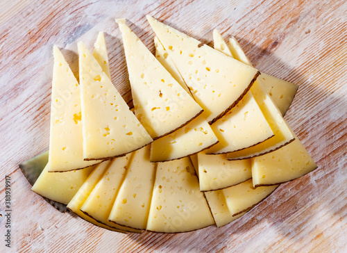 Slices of semi-hard cheese from milk of sheep on wooden background..