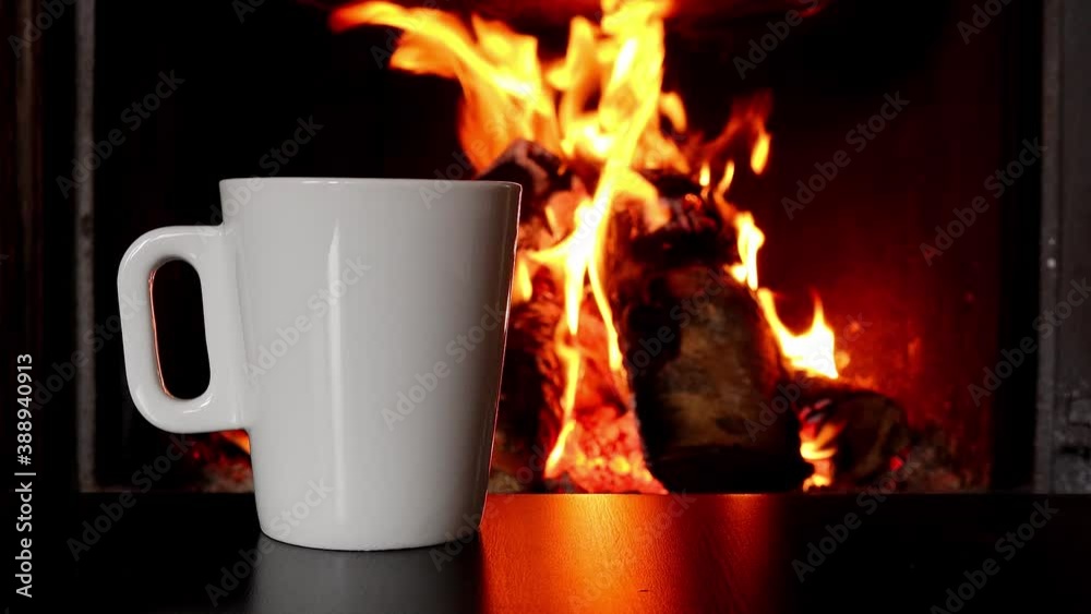Cup of coffee and birch logs of firewood in burning fire in fireplace, close-up Cup of coffee and birch logs of firewood in burning fire in fireplace, close-up