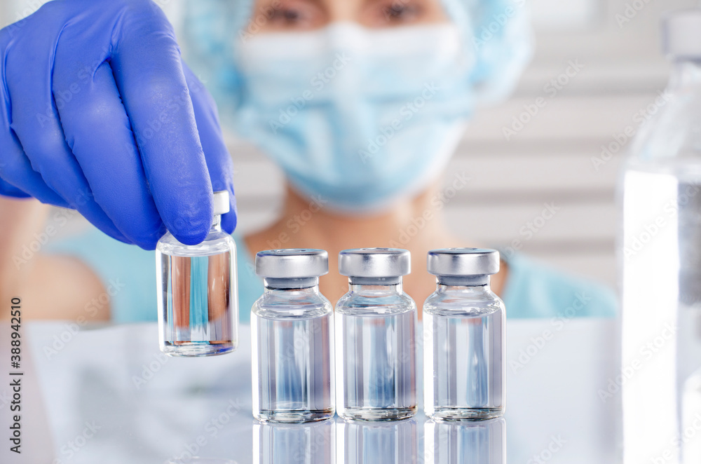 Female nurse in safety mask and gloves takes vial with liquid medicine from refrigerator shelf Female nurse in safety mask and gloves takes vial with liquid medicine from refrigerator shelf
