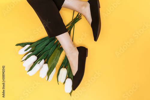 Beautiful female legs are dressed in stylish black flat shoes. black sandals on a yellow background