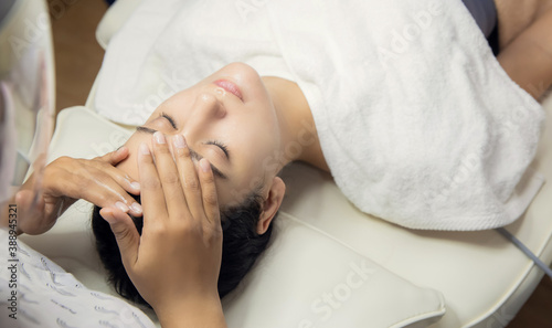 Relaxed woman lying in salon and having deep cleansing nourishing facial treatment. Beautician applying cream and doing face massage to client face. Healthcare, wellness and medicine