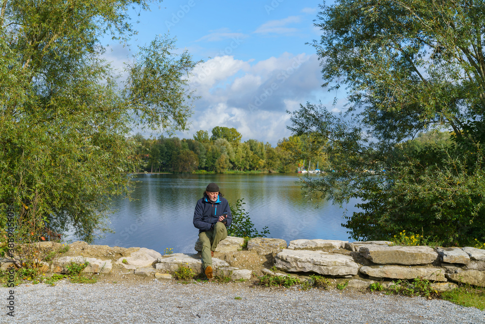 A man sitting on stones on the shore of the lake with a smartphone. A man sitting on stones on the shore of the lake with a smartphone.