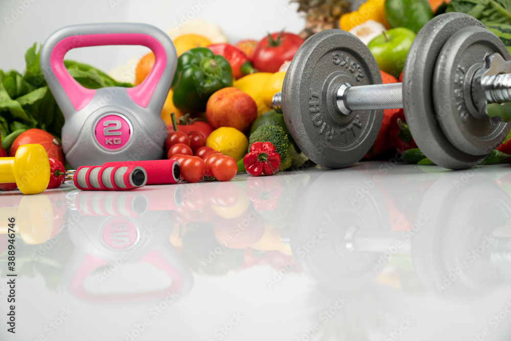 Fototapeta premium Fitness concept. Healthy nutrition: fruits and vegetables. Equipment for fitness exercises: weighing machine and dumbells. White background.