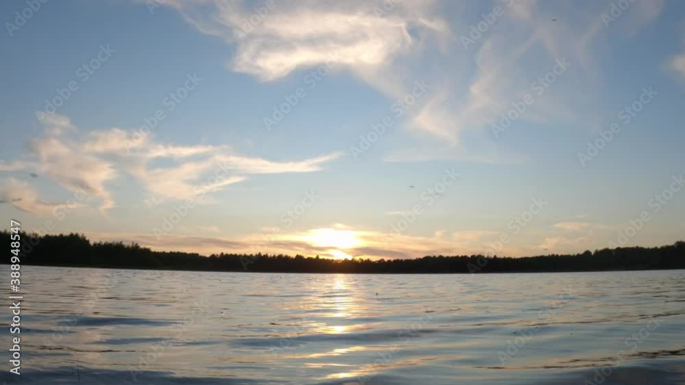 Beautiful sunset and cloudy sky over a forest lake at evening in vacation, showing the gentle lake ripples and waves at sunset, with a slow pan, revealing the reflection of the setting sun. High Beautiful sunset and cloudy sky over a forest lake at evening in vacation, showing the gentle lake ripples and waves at sunset, with a slow pan, revealing the reflection of the setting sun. High