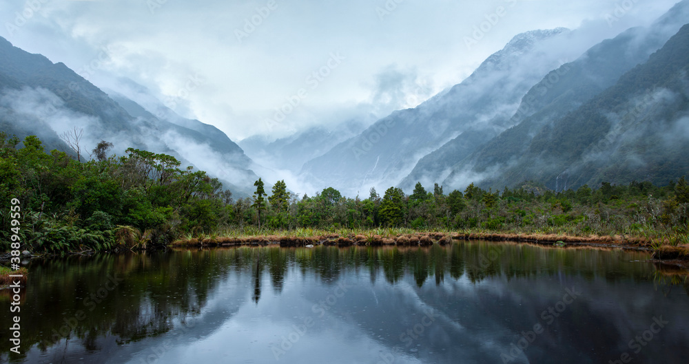 Franz Josef Glacier valley and mountains reflected in Peter's pool in the rain, South Island, New Zealand