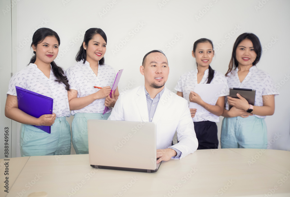 Portrait of confident asian medical team looking away. Female nurses or students standing around male doctor or teacher in clinic office or hospital room Portrait of confident asian medical team looking away. Female nurses or students standing around male doctor or teacher in clinic office or hospital room