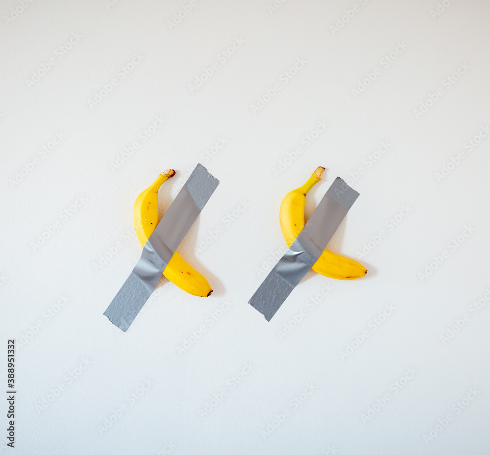 Two bananas taped to the white wall.