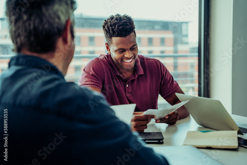 African business male manager with colleague looking at paper work discussing plans for new venture, in conference room photo