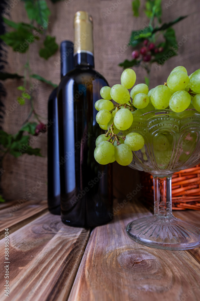 Obraz premium Two bottles of red and white wine on a wooden table with a bunch of grapes.