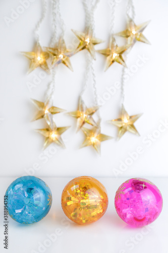 Three colorful christmas balls and some star shaped lights against white background. Copy space..