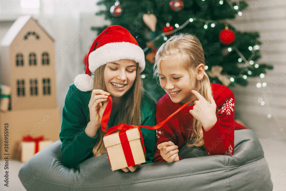 Two happy and beautiful teenage girls in New Year's outfits open gifts at home under the Christmas tree. Christmas mood. Concept for New Years holiday at home. Two happy and beautiful teenage girls in New Year's outfits open gifts at home under the Christmas tree. Christmas mood. Concept for New Years holiday at home.