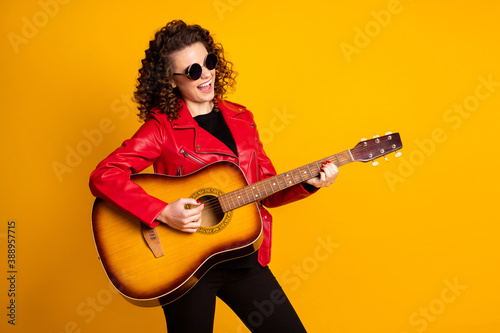 Portrait of pretty cheerful talented famous wavy-haired girl playing guitar isolated on bright yellow color background