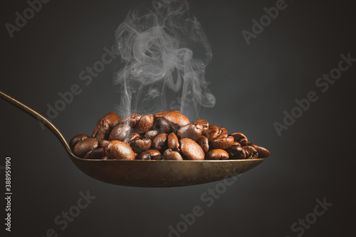 A spoon full of roasted coffee beans on black background