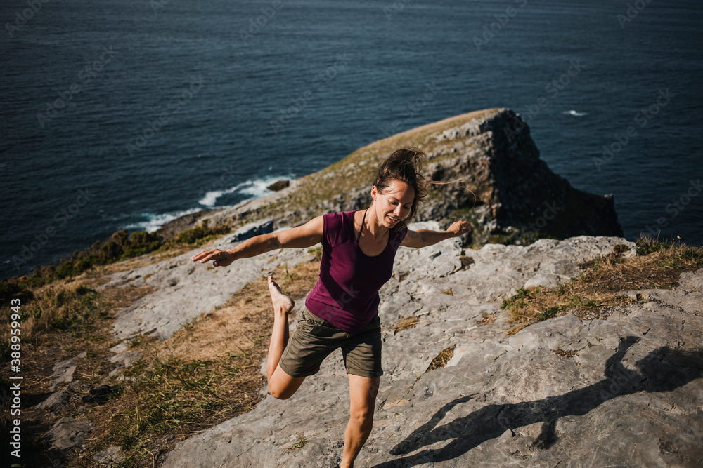 Woman jumping and dancing in front of a cliff with the ocean in the background.