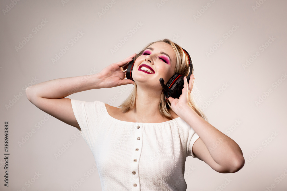 Happy blonde woman with bright makeup and headphones enjoys music on a simple background Happy blonde woman with bright makeup and headphones enjoys music on a simple background