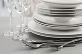 Stacked plates, cutlery and glasses on light grey table, closeup