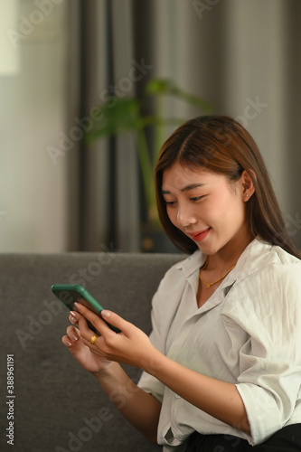Portrait of a young woman using smart phone while sitting on couch at home.