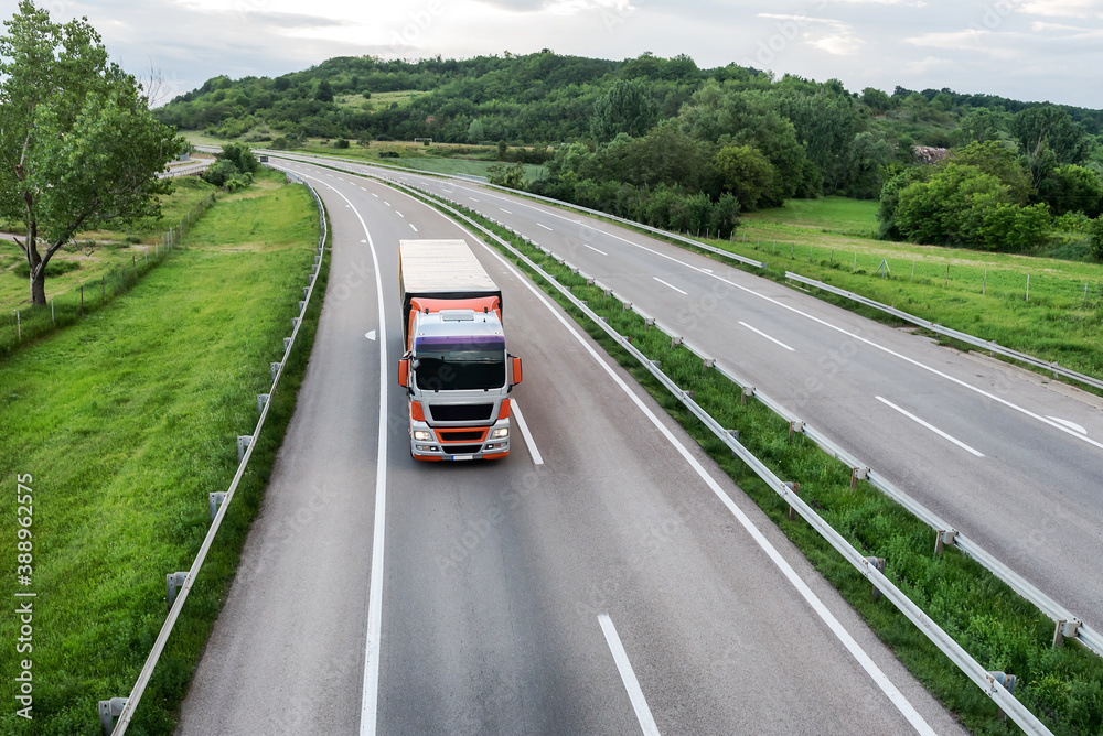 Fototapeta premium Big transportation truck on an Asphalt highway road or highway closeup against the background of rurallandscape with green fields and forest on the horizon of blue sky