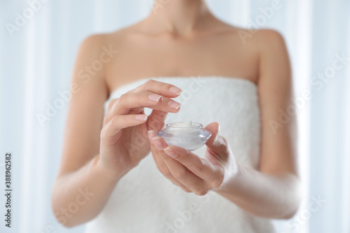 Young woman holding glass jar of cream at home  closeup
