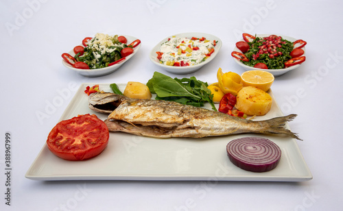 Bluefish and appetizers in white plate, standing on isolated background.