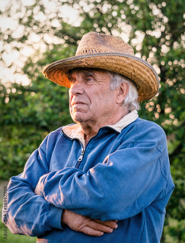 Elderly man in a straw hat on the background of the evening summer garden	