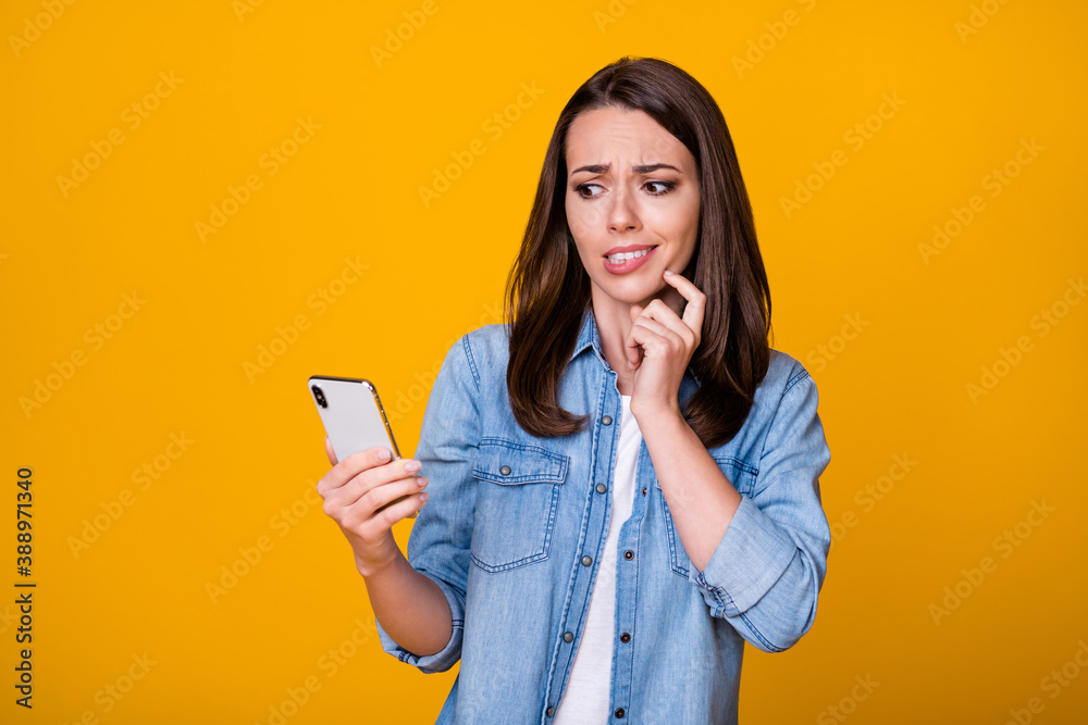 Photo of attractive youngster lady hold telephone biting lips displeased reading blog negative comments unhappy sad wear casual denim shirt isolated bright yellow color background Photo of attractive youngster lady hold telephone biting lips displeased reading blog negative comments unhappy sad wear casual denim shirt isolated bright yellow color background