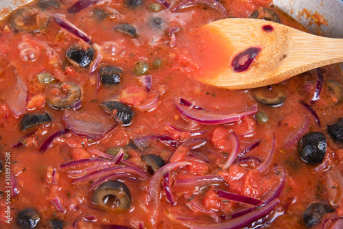 Cooking spaghetti alla vesuviana, pasta with sauce and tomatoes, olives, onions and capers - Cooking sauce from onions, chopped tomatoes, olives and capers in a frying pan close-up photo