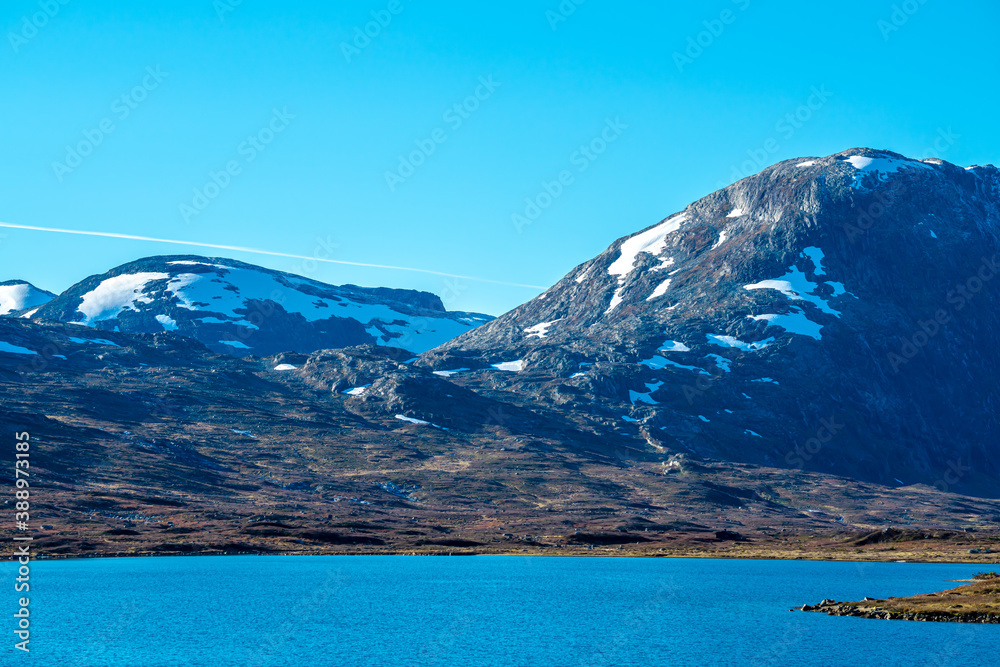 Tall snow covered mountain peaks and a clear blue glacial lake in the valley.