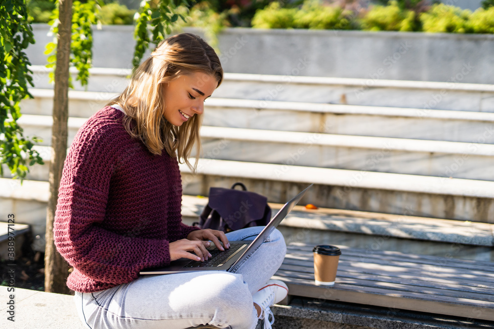 Young woman working with a laptop sitting in a bench in a park