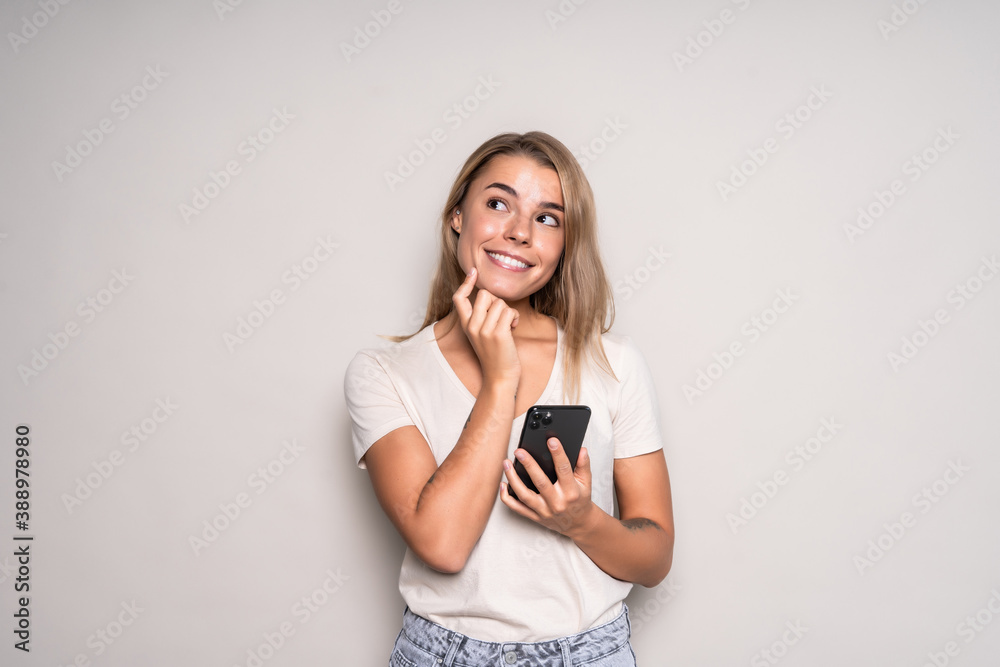 Portrait of a thoughtful young woman holding mobile phone and looking up at copy space isolated over white background Portrait of a thoughtful young woman holding mobile phone and looking up at copy space isolated over white background