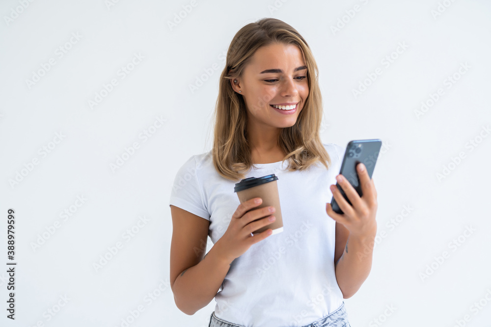 Portrait of a satisfied young woman using mobile phone while holding cup of coffee to go isolated over white background Portrait of a satisfied young woman using mobile phone while holding cup of coffee to go isolated over white background
