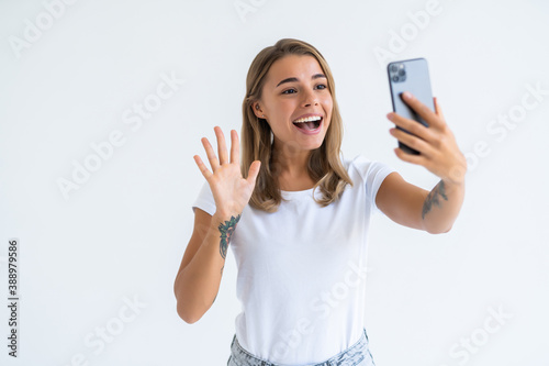 Happy young woman blogger influencer holding modern smart phone wave hand hello. Smiling vlogger girl looking at mobile make video call, shooting vlog taking selfie on white background