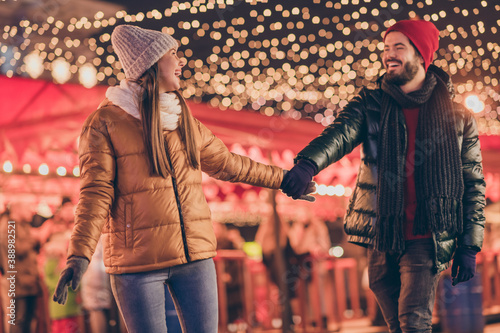 Photo of couple walk christmas evening town fair hold hands x-mas outside lights everywhere shine wear season outerwear