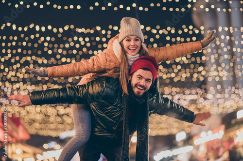 Photo of couple having fun evening outside x-mas christmas event boyfriend hug piggyback girlfriend hold hands fly illumination newyear around fair