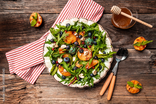 Easy recipe for summer salad with goat cheese, grilled apricots, arugula, berries, close-up on a plate wooden background, recipe top view photo