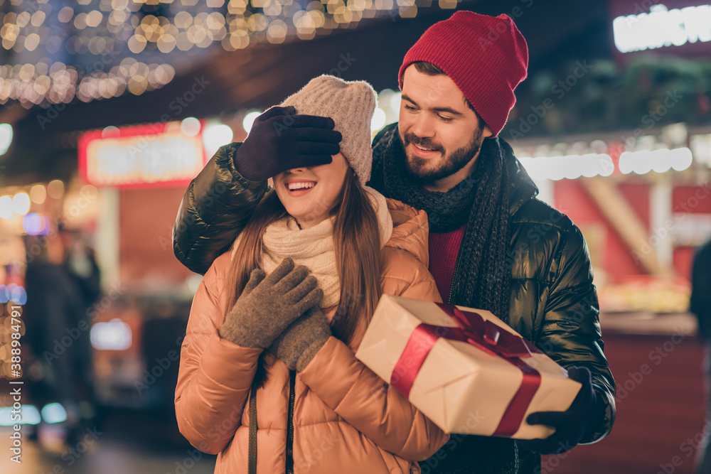 Photo of two people students couple boy cover hand girlfriend eyes give x-mas gift box amaze outdoors illumination lights around