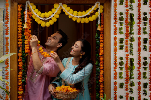 A HUSBAND AND WIFE HAPPILY DECORATING HOUSE WITH FLOWERS FOR DIWALI	 photo