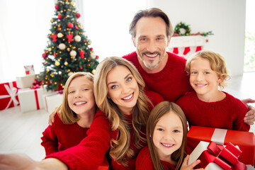 Photo of full big family five people meeting three little kids hold present box bow ribbon mom make shoot selfie wear red jumper in living room x-mas tree lights many gifts indoors