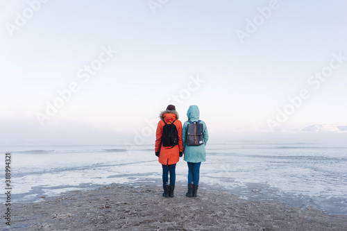 two girls in bright winter jackets do not admire the sweeping sea on the snowy shore beyond the Arctic Circle on a frosty winter day