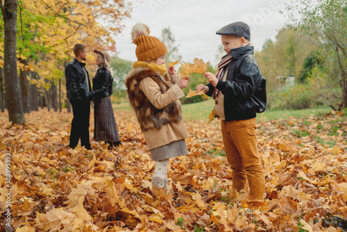 children play actively with leaves, autumn park. boy and girl hugging.