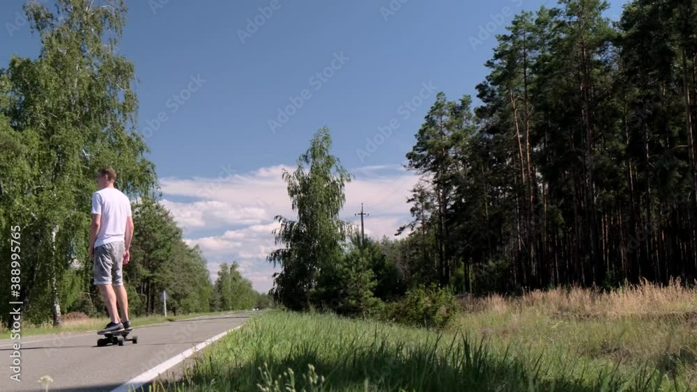 Young adult sports man skateboards on the road in the middle of a pine forest Young adult sports man skateboards on the road in the middle of a pine forest