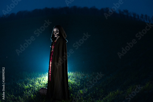 Woman stands in Halloween costume of death against dark sky.