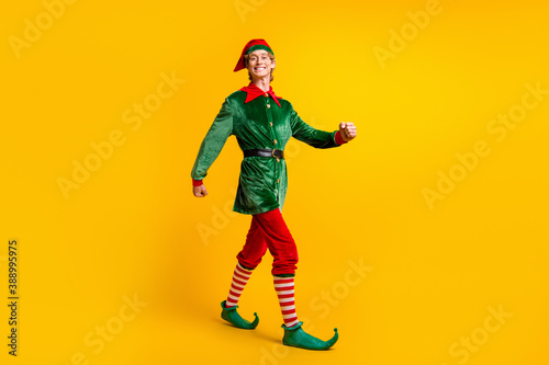 Full length body size view of his he nice attractive cheerful cheery funny guy elf walking having fun christmastime winter party isolated over bright vivid shine vibrant yellow color background
