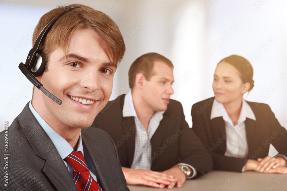 A smiling young businessman call center agent wears a wireless headset at the workplace. A smiling young businessman call center agent wears a wireless headset at the workplace.