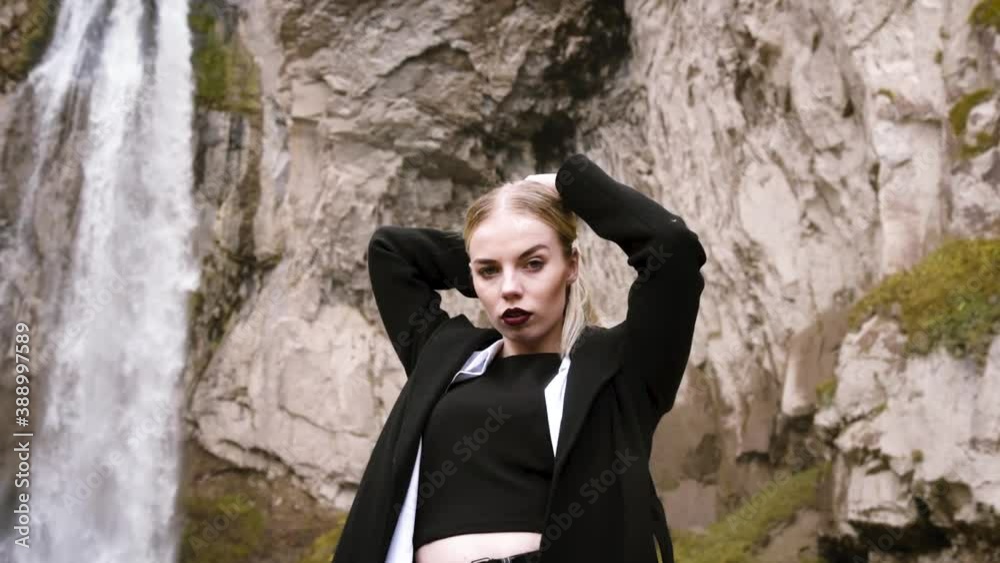 Beautiful blonde woman on the background of a large waterfall high in the mountains in autumn, beautiful autumn scenery and mountain views. Video in HD quality Beautiful blonde woman on the background of a large waterfall high in the mountains in autumn, beautiful autumn scenery and mountain views. Video in HD quality