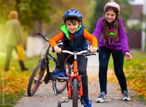 Autumn day. Sister teaches her little brother to ride a bike and rejoices at his success. Family and healthy lifestyle