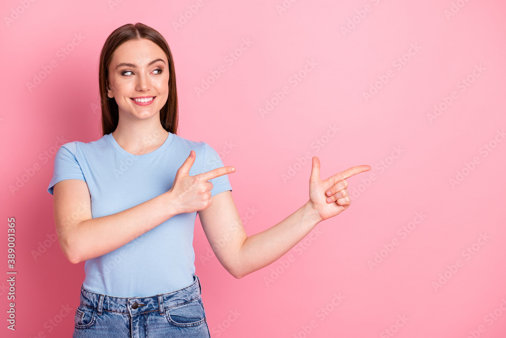 Photo portrait of woman pointing to fingers looking to side isolated on pastel pink colored background Photo portrait of woman pointing to fingers looking to side isolated on pastel pink colored background