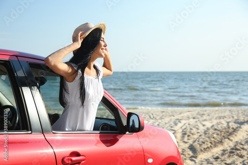 Happy young woman leaning out of car window on beach, space for text. Summer trip © New Africa